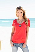A young woman on a beach wearing a red top and jeans