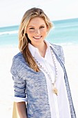 Junge Frau in weisser Bluse und Strickjacke am Strand