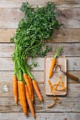 Fresh carrots next to a carrot on a chopping board with a vegetable peeler