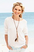 A young woman on a beach wearing a white jumper and light-blue shorts