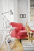 A dog jumping off a red armchair with a reading lamp and a tray table