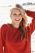 A young woman on a beach wearing a rust-red jumper