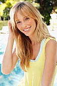 A young blonde woman by the pool wearing a yellow summer dress