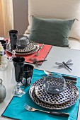 Table set with colourful mats, spotted plates and black drinking glasses