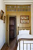 Antikes Messingbett vor Holzwand mit Oberlicht und offener Zimmertür, Blick auf Holzschrank im Flur