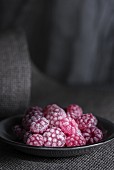 Raspberry sweets in a grey plate on a piece of grey fabric