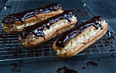 Chocolate eclairs filled with cream and topped with chocolate glaze on a wire rack