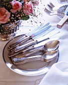Silver cutlery on a white plate next to a bunch of roses in a silver vase