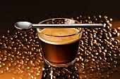 Glass of espresso with a spoon on a reflective surface with coffee beans