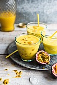 Three glasses of passion fruit smoothie with straws on a grey metal plate