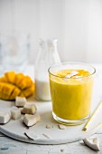 A glass of mango and coconut smoothie with chunks of fresh coconut, coconut milk and mango