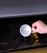 A cup of water being poured on to a hot baking tray for steaming