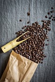 Coffee beans spilling from a paper bag with a bamboo scoop on a grey linen cloth