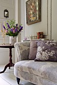 Floral scatter cushions on floral sofa in front of vase of flowers and floral painting