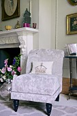 Elegant easy chair with silver velvet cover next to open fireplace