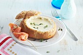 Cheese fondue served in a hollowed out loaf of bread with a salmon skewer