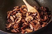 Brown mushrooms being fried with chopped garlic in olive oil in a wok