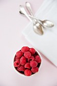 Raspberries in a white bowl on a pink tablecloth