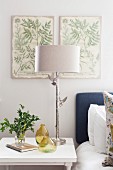 Bedside lamp with silver base and two bird ornaments below botanical illustrations on wall