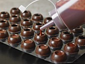 Hollow chocolate balls being filled with fruit ganache from a bottle