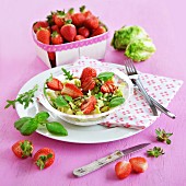 A salad with strawberries, a punnet of strawberries and lettuce in the background