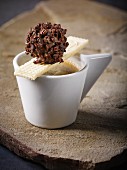 A homemade nougat truffle in dark chocolate with cocoa bean splinters on a cup of espresso with a wafer