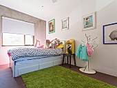 Girl with dog on bed in children's room with concrete wall and flea market items