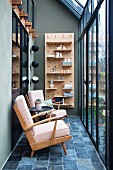 Two retro armchairs in front of wall-mounted shelved in glass house