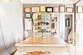 Antique dining table and white metal chairs inn front of gallery of pictures and mirrors on grey wall