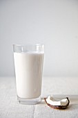 A glass of coconut milk next to a slice of coconut
