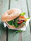 A bagel with trout fillet, tomatoes and rocket