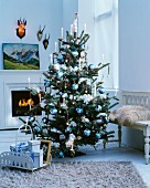Elegant geschmückter Weihnachtsbaum mit blau-weißen Christbaumkugeln vor Kamin