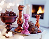 Colourful metallic candlesticks and artistically decorated baubles on tray next to bowl of fruit
