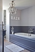 Elegant bathroom in shades of grey with panelled bathtub and chandelier