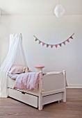 Free-standing bed below canopy in front of bunting on wall
