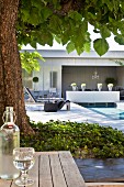 Flasche und Glas mit Wasser, Baum und Liegen am Pool