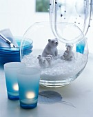 Polar bear figurines and artificial snow in glass vase next to tealights in blue glasses