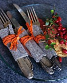 Silver cutlery wrapped in felt and raffia on glass plate