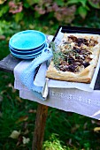 A puff pastry tart with braised radicchio and shallots on a table in a garden