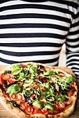 A pizza with tomatoes, basil and rocket on a wooden board