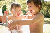 Little boy and little sister playing with water in garden