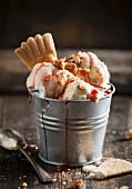 Three scoops of vanilla ice cream with strawberry sauce, nuts and a wafer in a zinc bucket