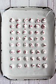 Mini meringues decorated with dried raspberries on baking paper (seen from above)