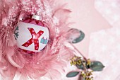 Painted Christmas bauble surrounded by delicate pink feathers