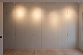 Floor-to-ceiling, minimalist fitted cupboards lit by spotlights