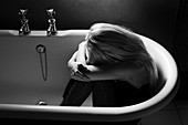 Depressed young woman in an empty bathtub