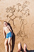 Boy lying with his drawings in the sand