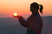 A woman holding the setting sun