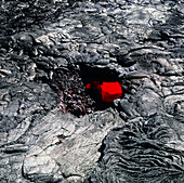 Red molten lava seen through a hole in lava tube