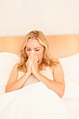 Woman in bed blowing nose on tissue